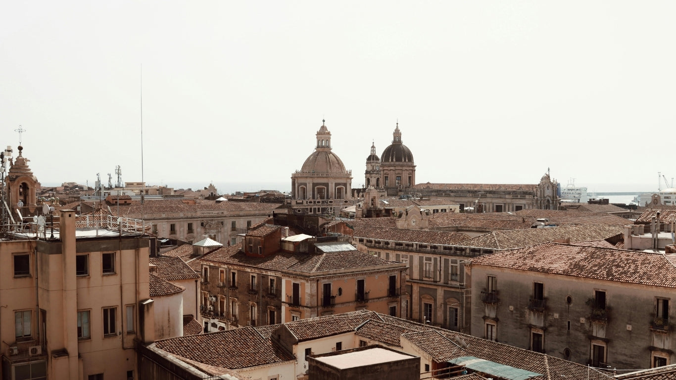 Photographie prise dans une ville en Sicile, avec une vue des immeubles et des toits de la ville avec, au centre, la coupole d'une église.