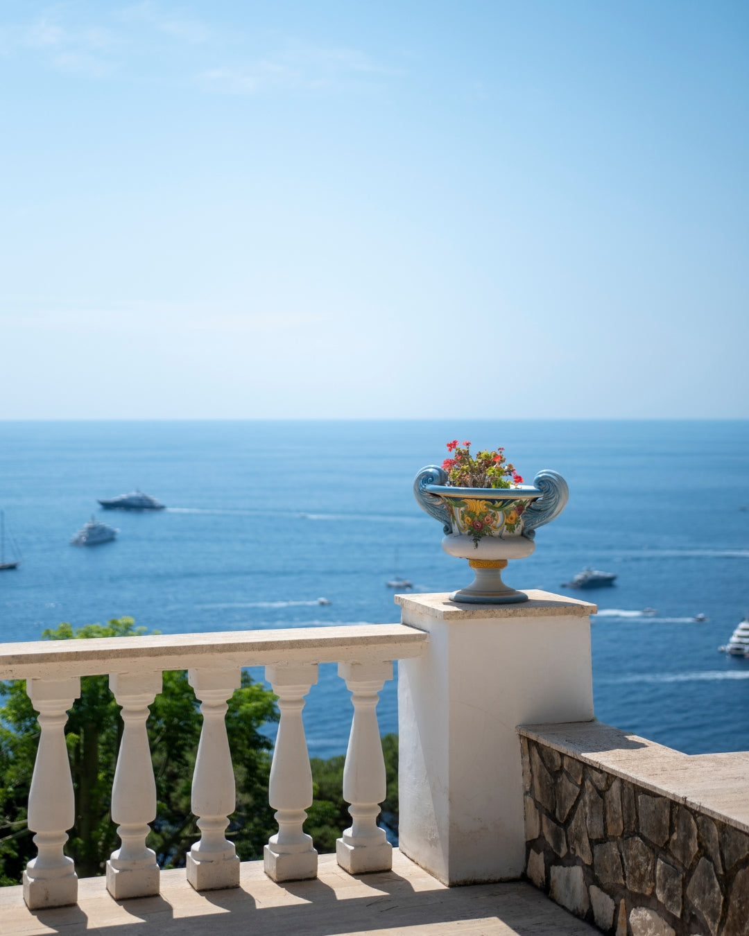 Vue d'un pot en céramique contenant des fleurs, sur un blacon, avec vue sur la mer en arrière-plan.