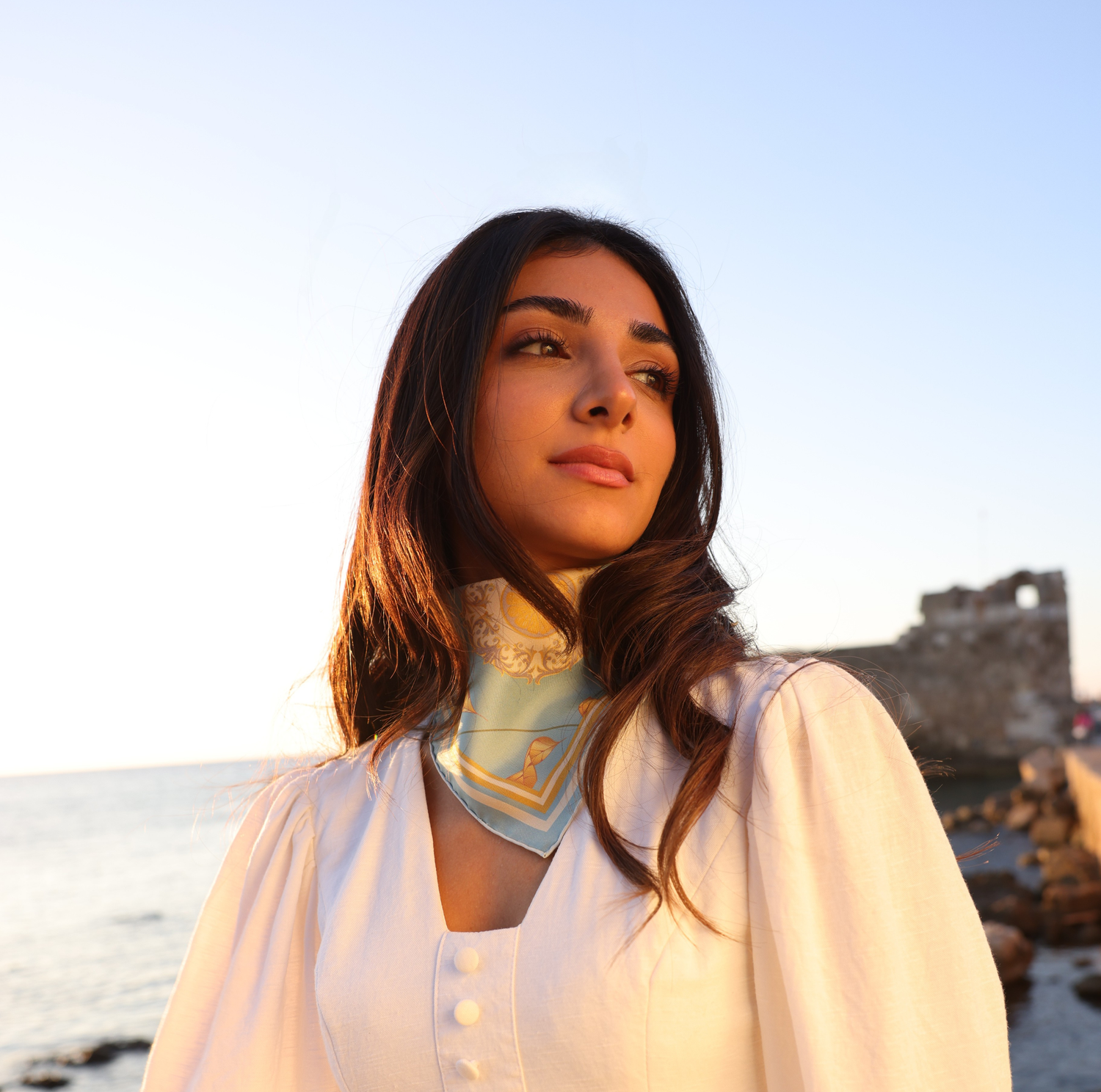 Foulard en soie porté autour du cou avec une vue sur la mer, avec la lumière dessus.