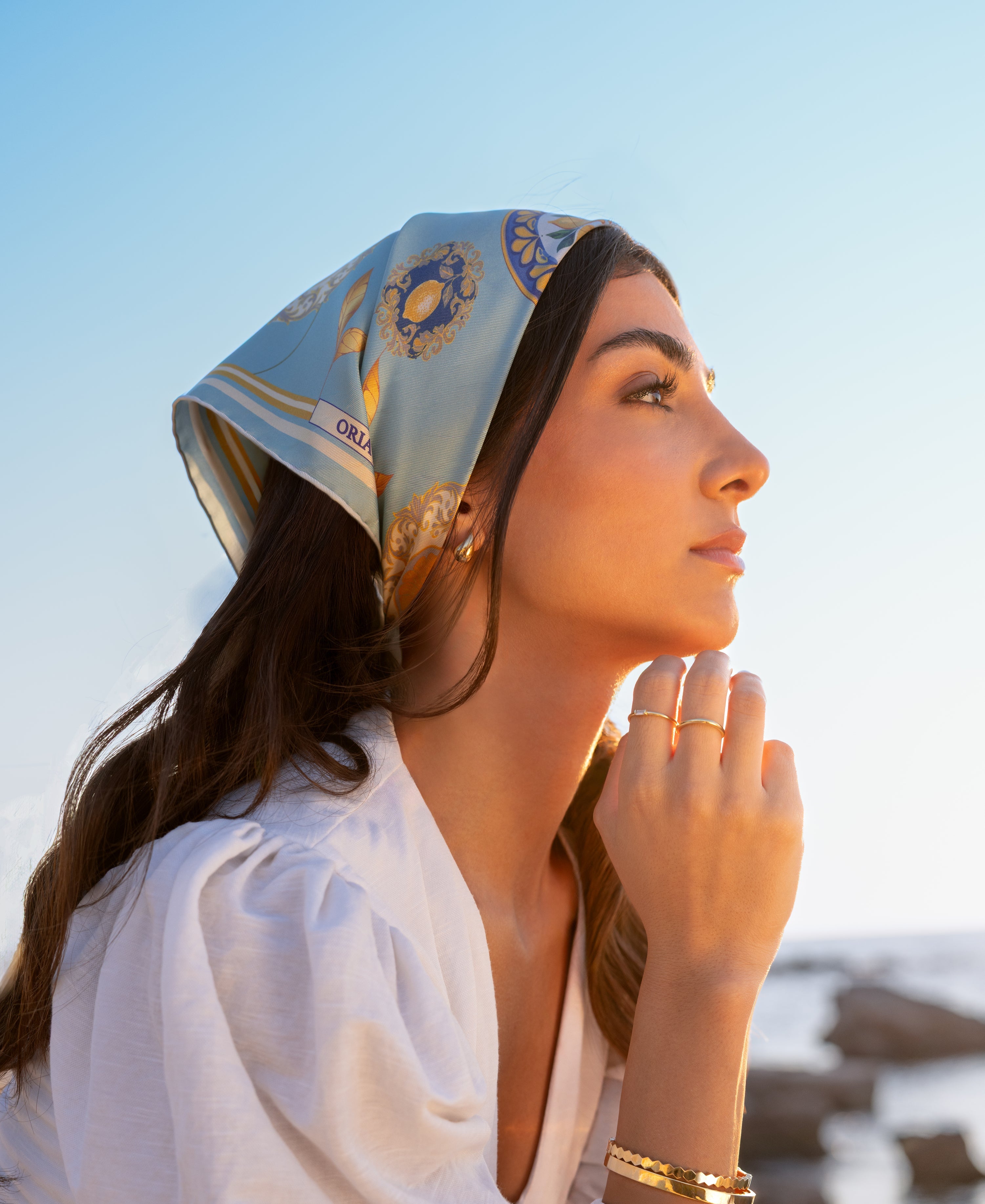 Foulard en soie porté sur les cheveux avec la mer en arrière-fond, dans une ambiance lumineuse.