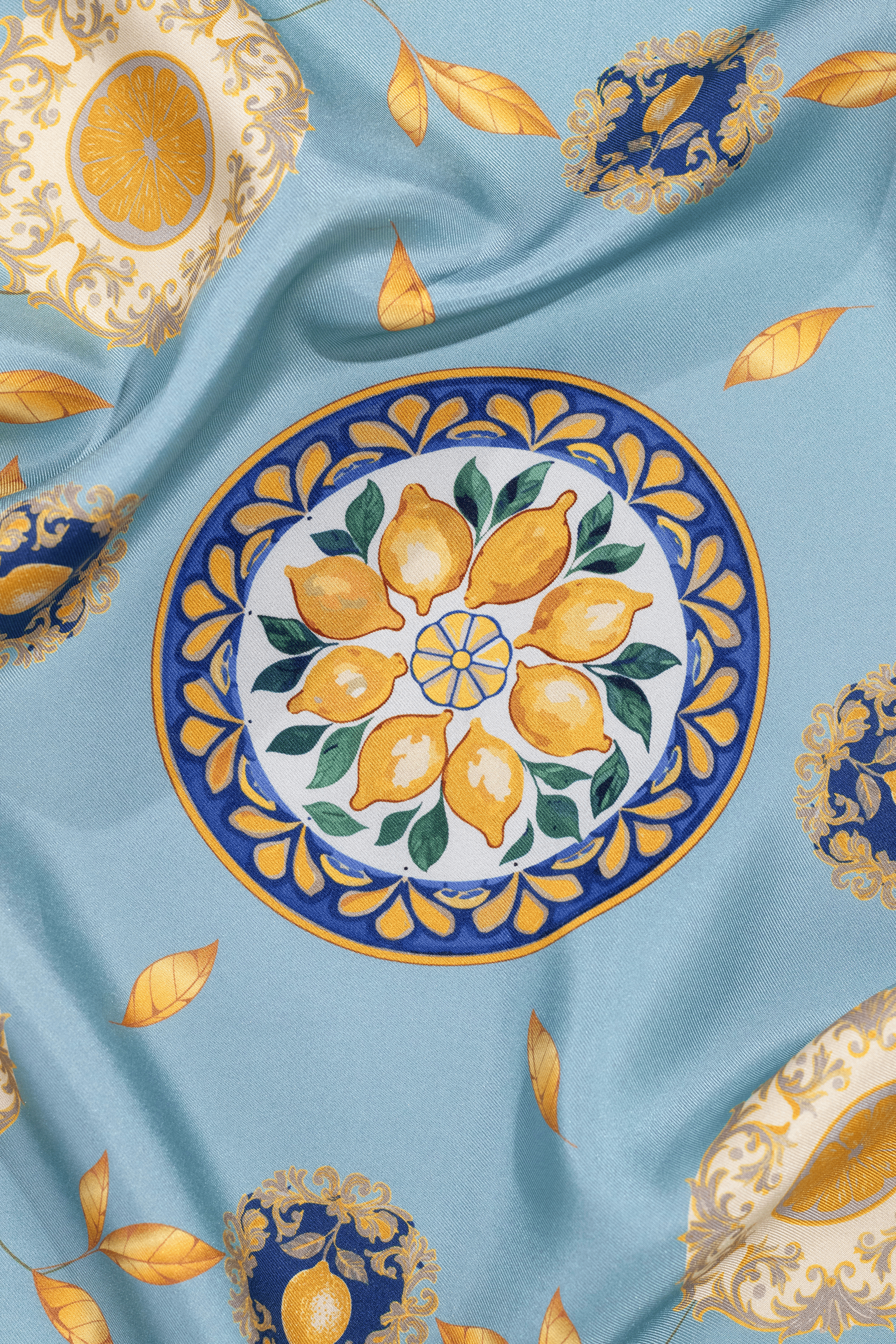 Vue des détails du foulard Capri Eleganza Bleu. Les motifs sont des citrons, des feuilles dorées et des références à la céramique de l'île de Capri.