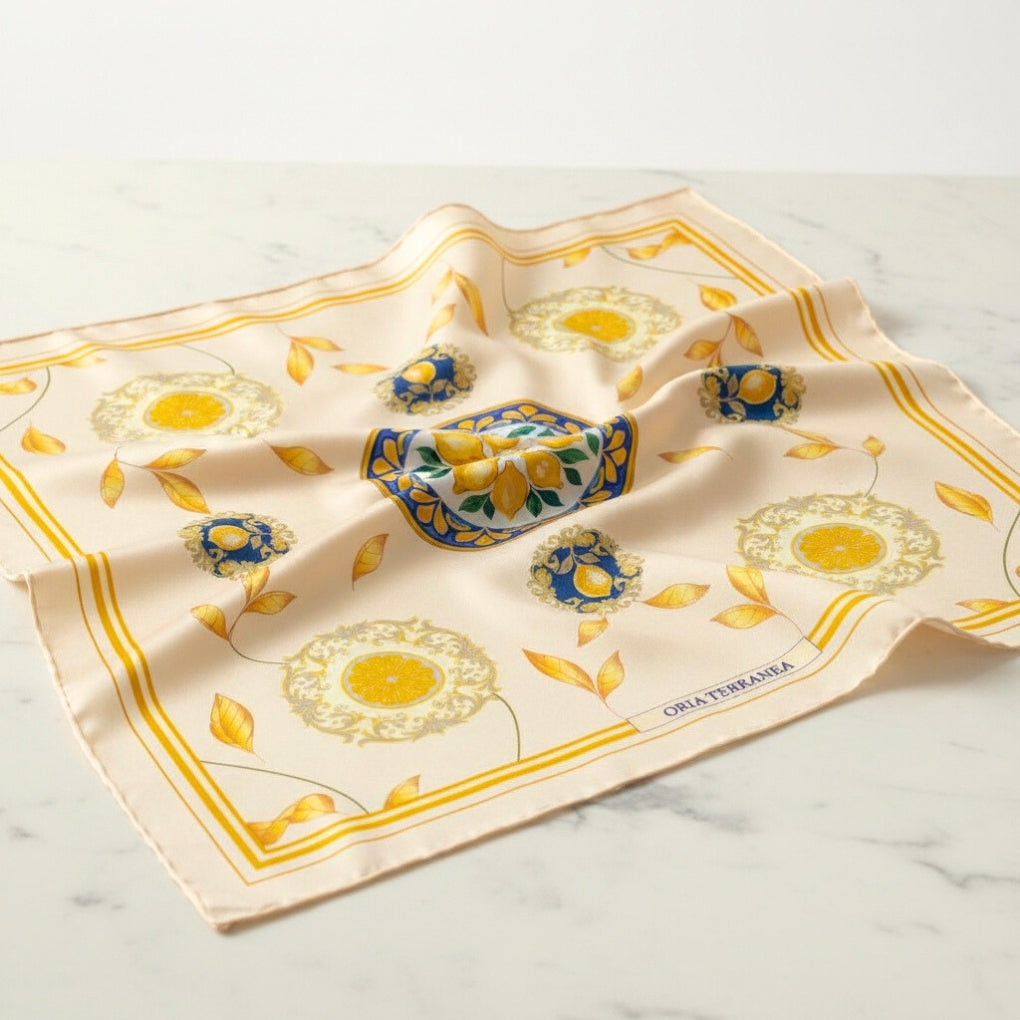 Vue du foulard Capri Eleganza Blanc sur du marbre, avec des motifs de citrons, feuilles dorées et des références à la céramique de l'île.